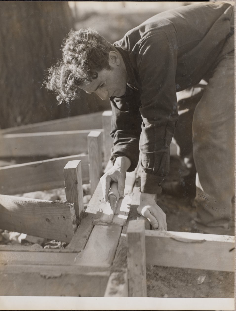 [Metselaar strijkt cement glad tijdens het storten van een fundering]. door Arnold Eagle