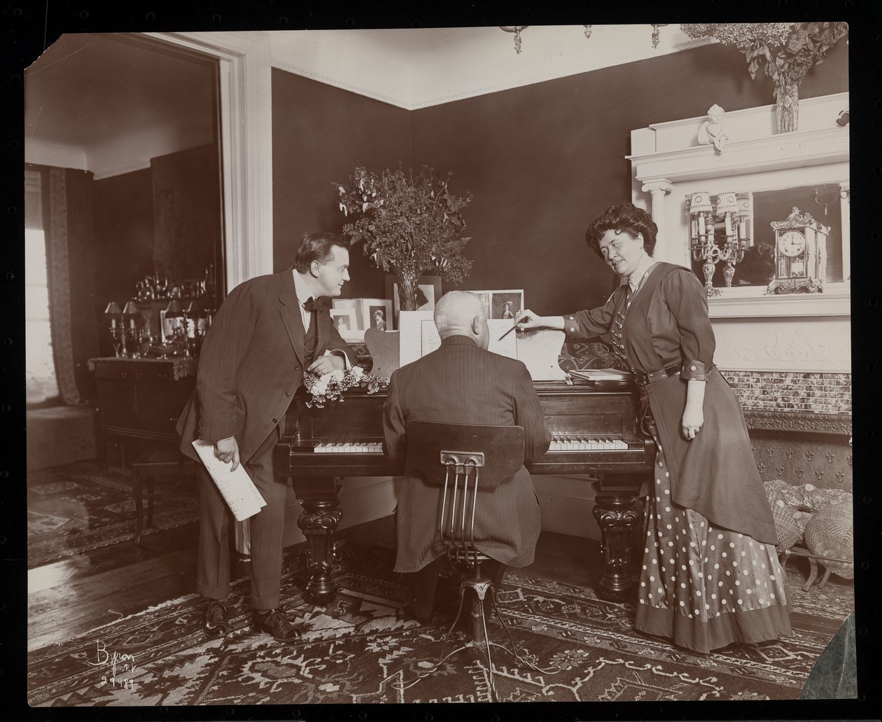 Clara De Regand wijst naar een partituur terwijl een man piano speelt, 1910 door Byron Company