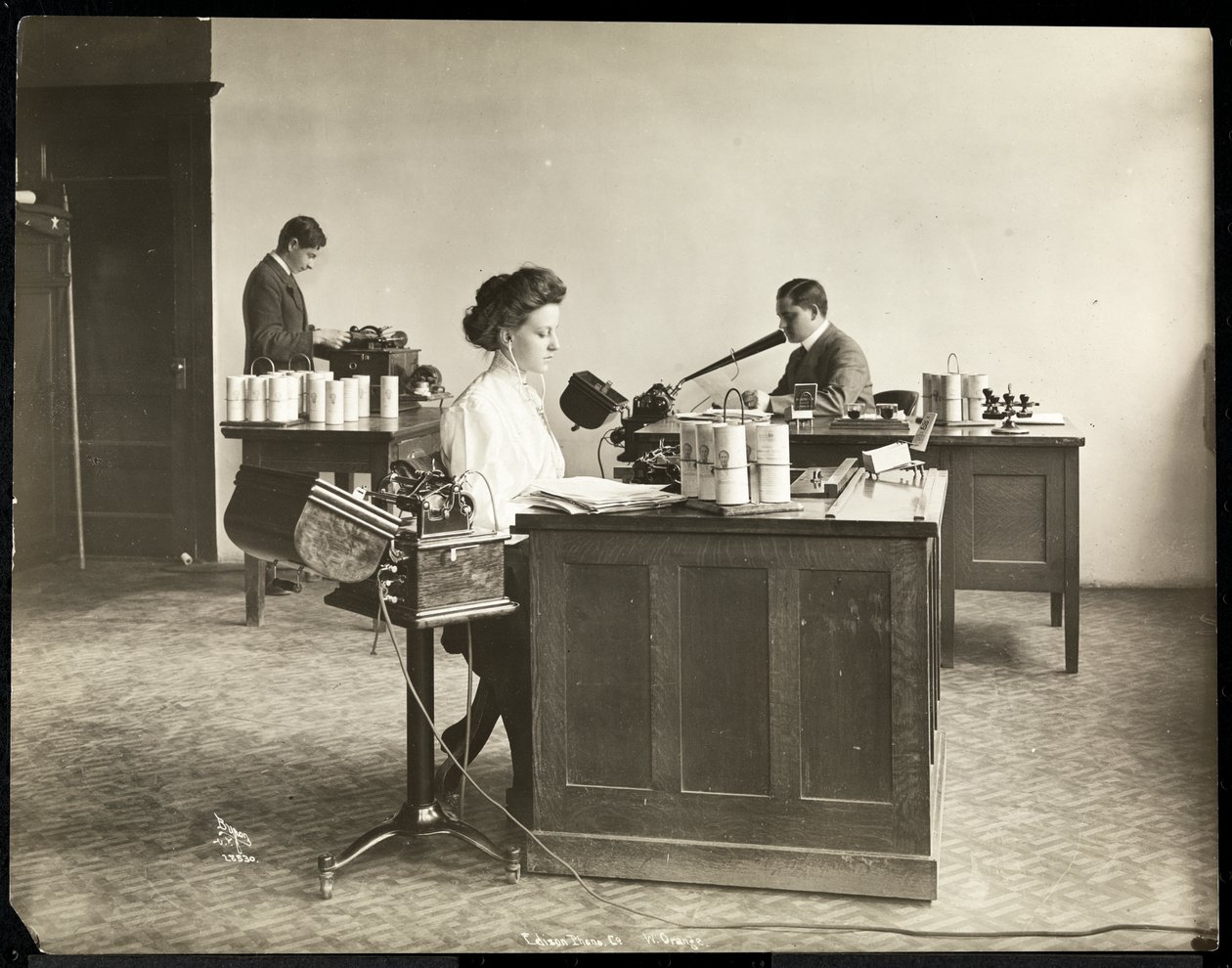 Interieur van een vrouw die typt vanaf een dicteermachine en een man die dicteert in een andere bij de Edison Phonograph Co., West Orange, New Jersey, 1903 door Byron Company