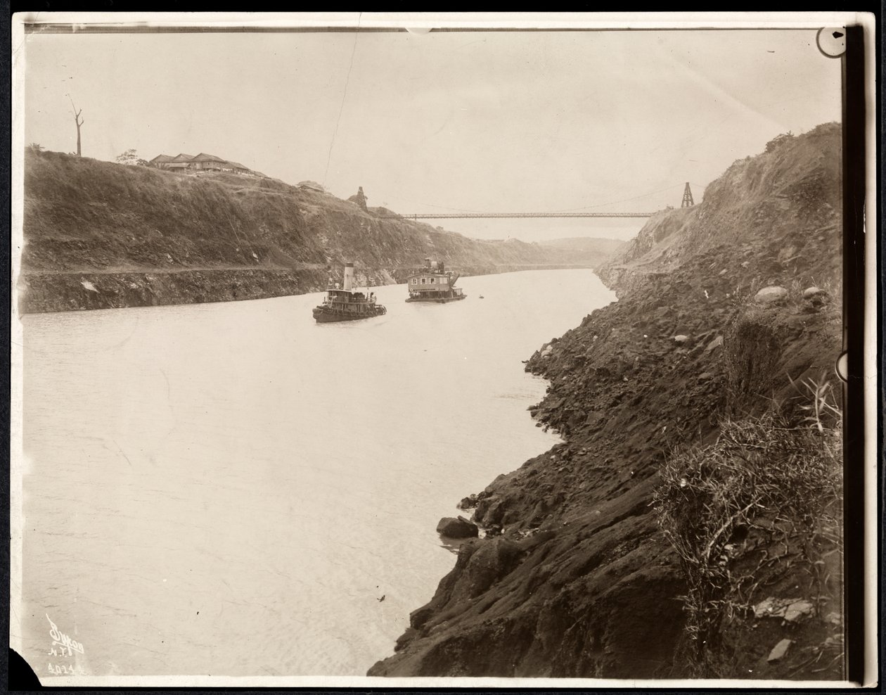 Uitzicht op twee boten in het Panamakanaal tijdens de bouw met een hangbrug daarachter, 1913 door Byron Company