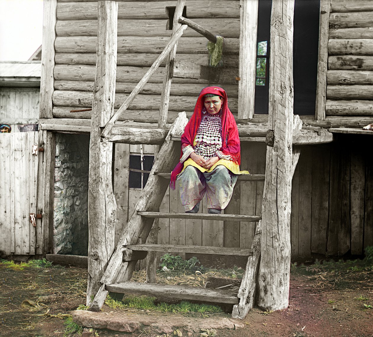 Bashkir vrouw in een volkskostuum zittend op de trap van haar houten huis, Oeralgebergte, Russische Rijk, 1910 door Sergey Prokudin Gorsky